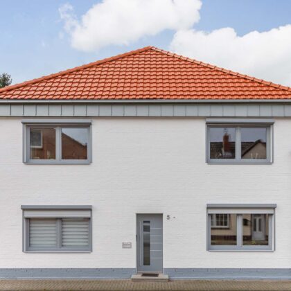 Vooraanzicht van een vrijstaand huis bedekt met moderne dakpan J160 in oudrood